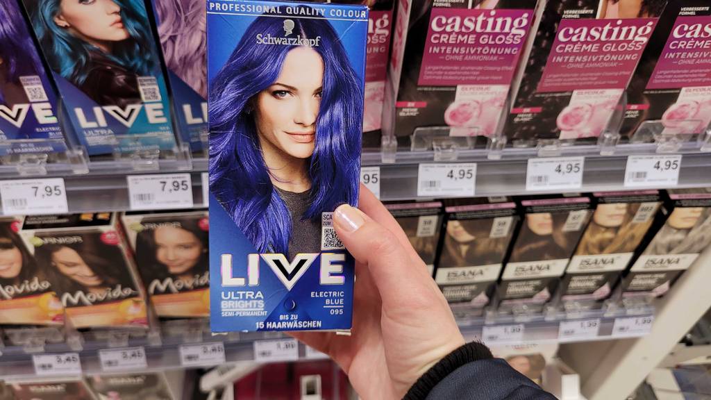 Im Test: Eine Hand hält eine Packung blaue Haarfarbe vor einem Regal mit Haarfarben.