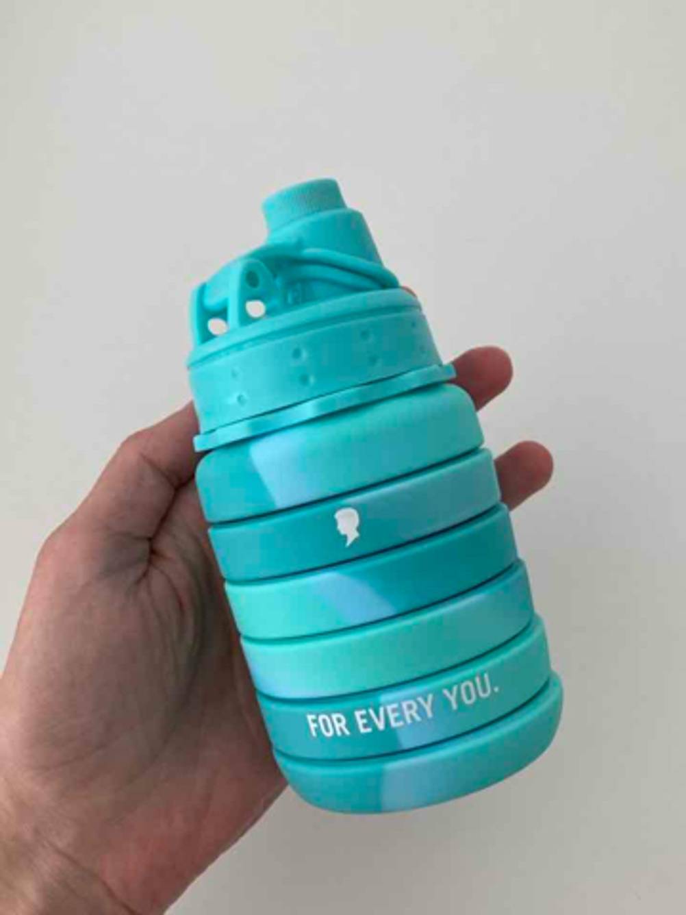 Faltbare Trinkflaschen im Test: Eine Hand hält die zusammengefaltete, türkisfarbene Kunststoffflasche vor einer weißen Oberfläche.