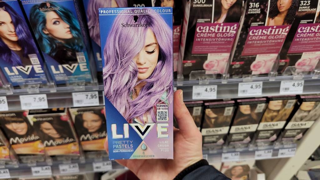 Im Test: Eine Hand hält eine Packung lila Haarfarbe vor einem Regal mit Haarfarben.