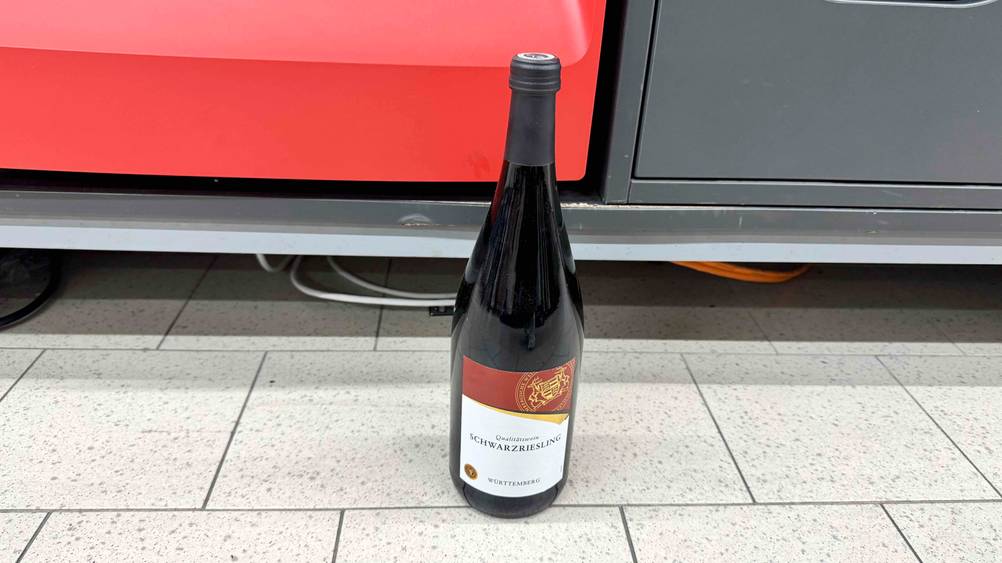Eine Flasche des getesteten Schwarzrieslings steht vor einem Regal auf dem Boden.