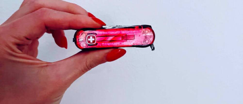 Eine Damenhand hält zwischen zwei Fingern ein rotes Schweizer Kindertaschenmesser im Test.