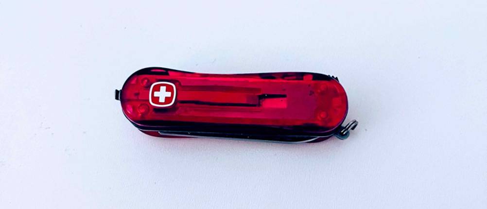 Kindertaschenmesser im Test: Auf einem roten Taschenmesser, das auf einer weißen Fläche liegt, ist das Logo für die Schweizer Taschenmesser eingedruckt.