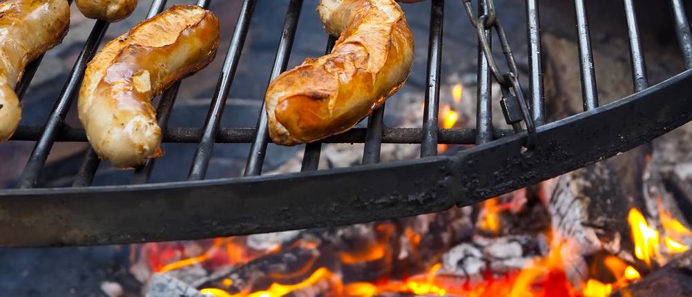 Würstchen werden auf Schwenkgrill über Feuer zubereitet.
