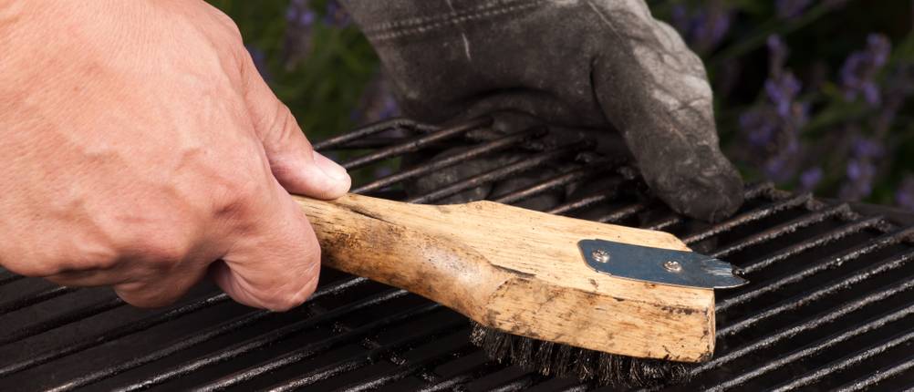 Benutzter Grillrost wird mit einer Drahtbürste gereinigt.