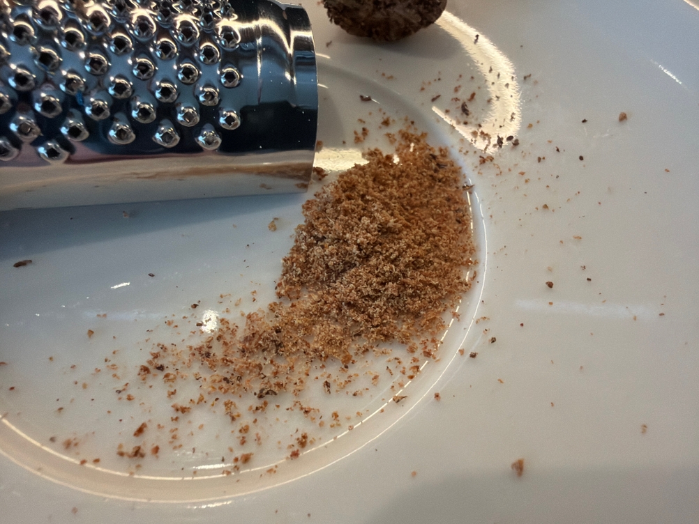 Geriebene Muskatnuss liegt neben der Schwertkrone-Muskatreibe