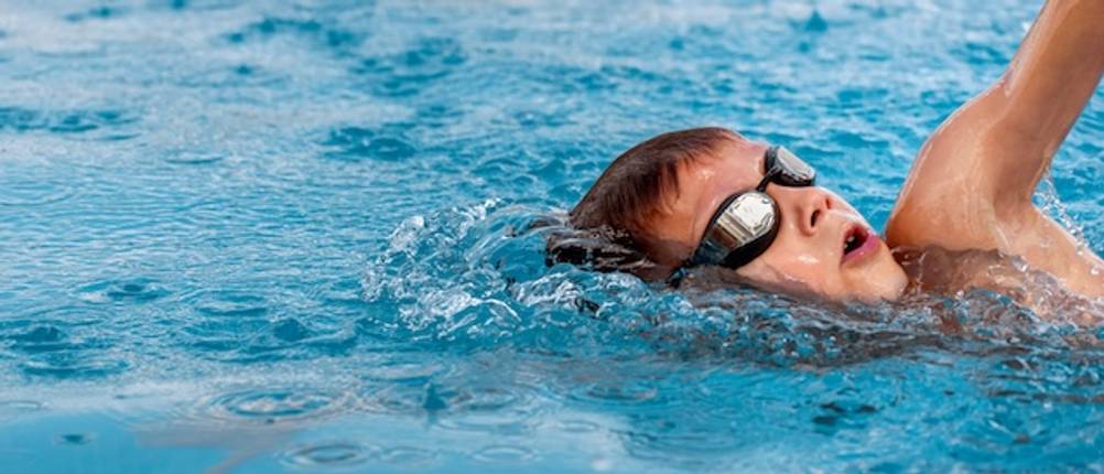 Pool-Schwimmgurt getestet: Ein Junge mit Schwimmbrille schwimmt in einem Pool.