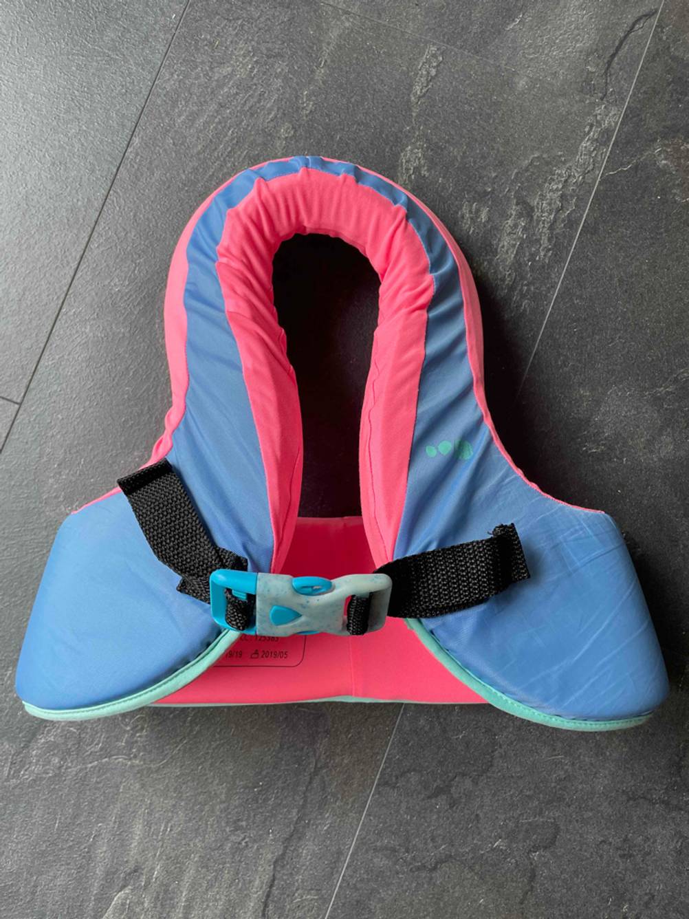 Eine getestete Schwimmlernweste von vorne auf einem dunklen Boden.