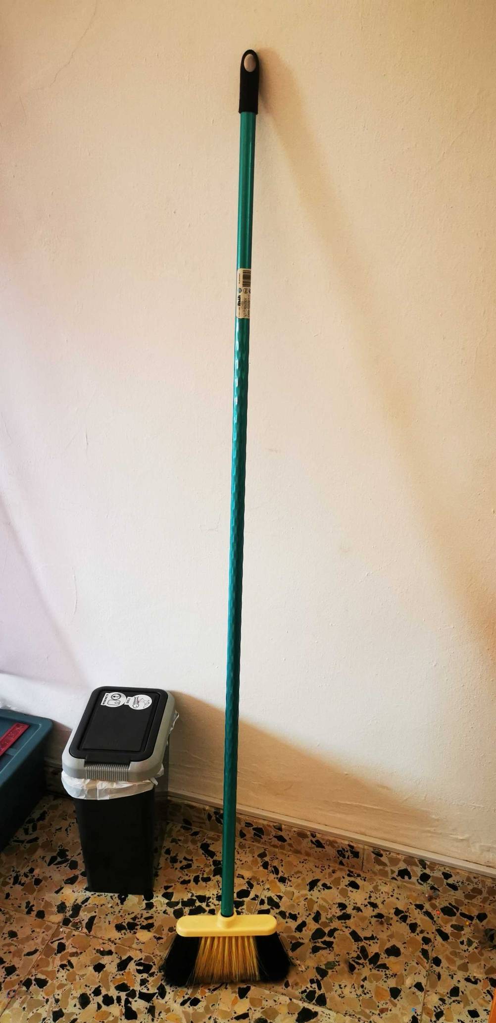 Ein getesteter Besenstiel steht mit Besen neben einem Mülleimer.