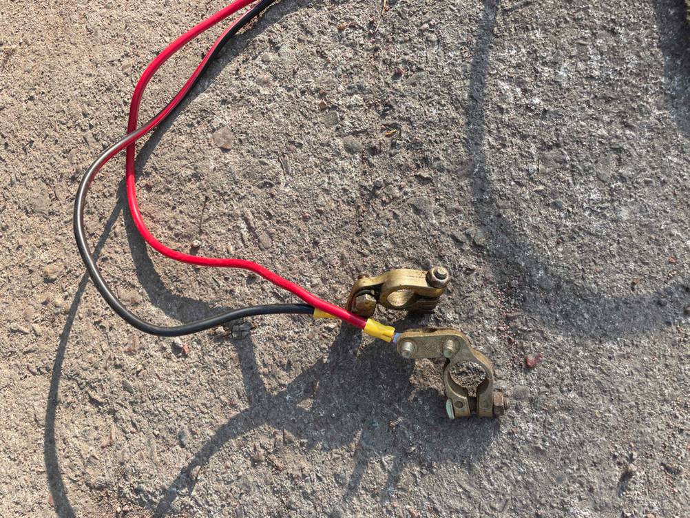 Nahaufnahme der Anschlusskabel einer getesteten Seilwinde 12 V an eine Batterie auf einem Steinboden.