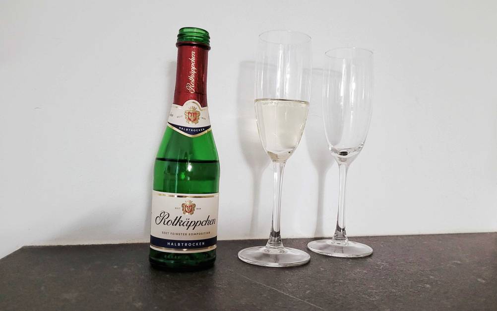 Eine Flasche des getesteten Sektes neben zwei Gläsern auf einer dunklen Fläche.