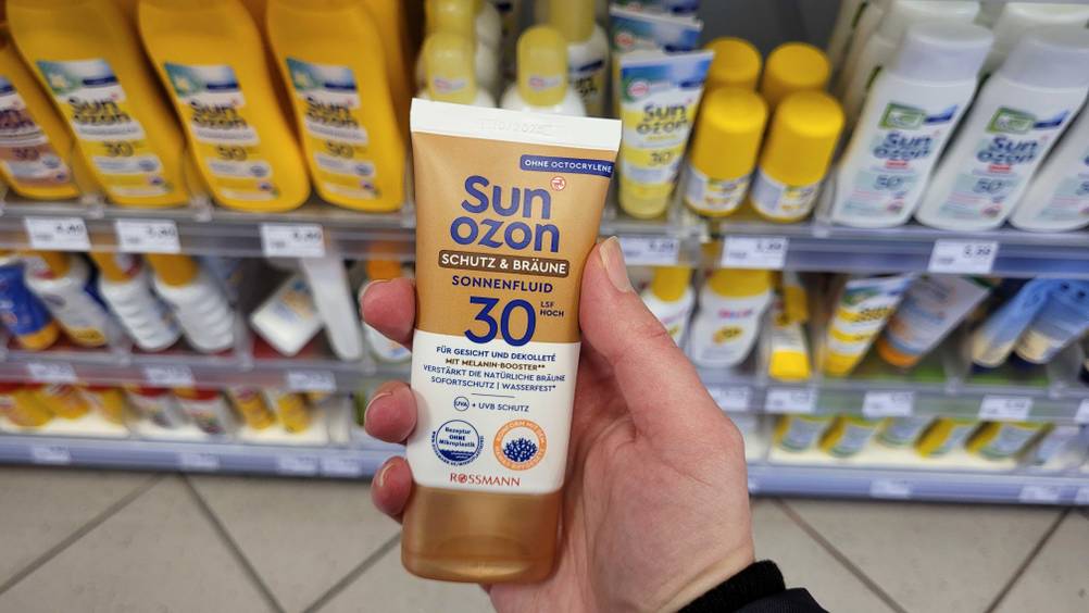 Im Test: Eine Hand hält eine Tube Selbstbräuner fürs Gesicht vor ein Regal.