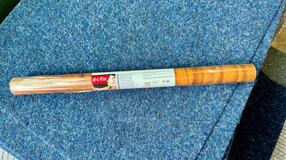 Selbstklebende Tapete im Test: Eine Rolle liegt horizontal auf eine blauen Matte.