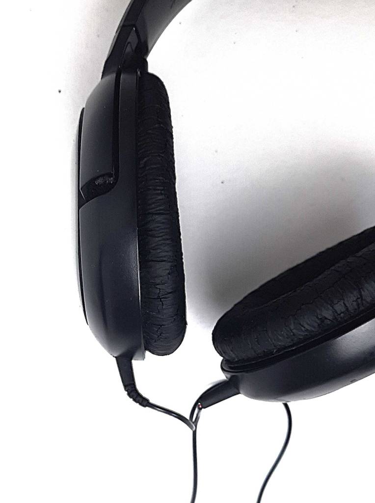 Detailansicht der gepolsterten Ohrmuscheln eines getesteten Sennheiser-Kopfhörers mit Kabel in schwarzer Ausführung auf einer weißen Oberfläche.
