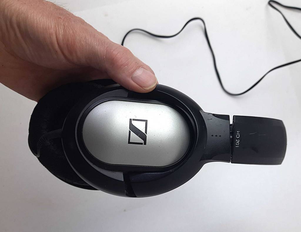 Eine Hand hält die gepolsterten Ohrmuscheln eines getesteten Sennheiser-Kopfhörers mit Kabel vor einer weißen Oberfläche.