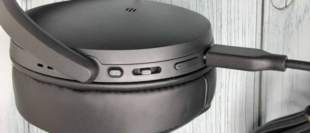 Noise-Cancelling-Kopfhörer im Test: Nahaufnahme eines Kopfhörers mit Fokus auf die integrierten Nutztasten sowie das angeschlossene USB-Kabel