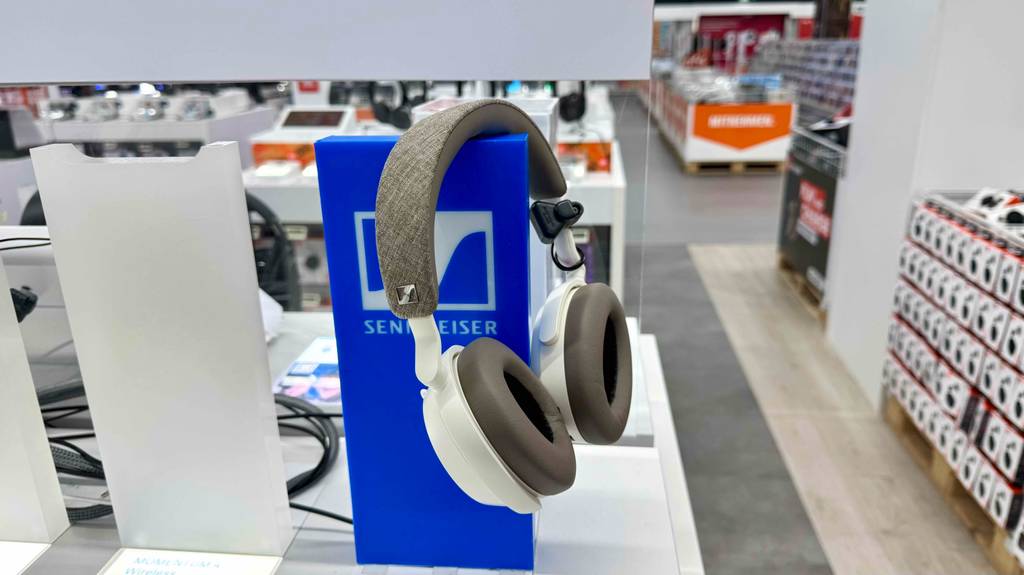 Seitenansicht von getesteten Sennheiser-Over-Ear-Kopfhörern, die über einem Markenschild hängen.