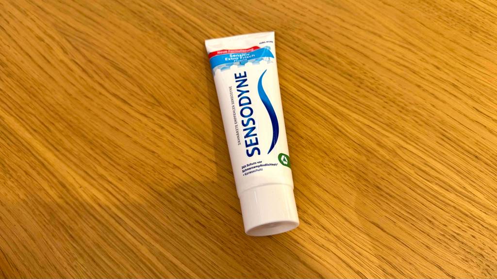 Eine Tube Sensodyne-Zahnpasta liegt zum testen auf einer Holzfläche.