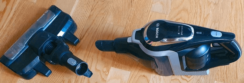 Bosch-Akkusauger im Test: Bosch Serie 8 BSS82SIL1 in dunklem Design liegt inklusive Boden-Saugdüse auf einem hellen Holzboden.