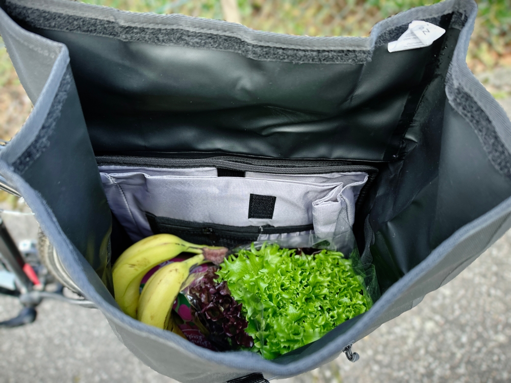 Innenansicht der Sevenrivers-Fahrradtasche mit frischem Obst und Gemüse. Im Hintergrund sind ein gepolstertes Laptopfach und Fächer sichtbar.