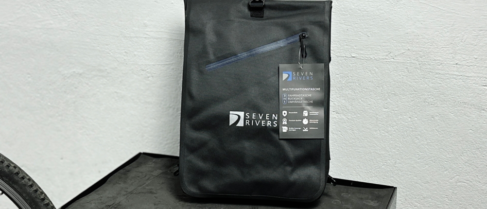 Die Sevenrivers-Fahrradtasche steht aufrecht vor einer weißen Wand und zeigt die Frontseite mit Logo und Reißverschlussfach. Das Etikett mit Produktinfos ist noch befestigt.