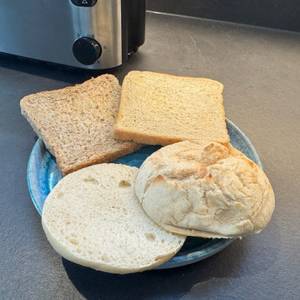 Auf einem Teller liegen ein geschnittenes Brötchen, ein Weizentoast und ein Vollkorntoast.