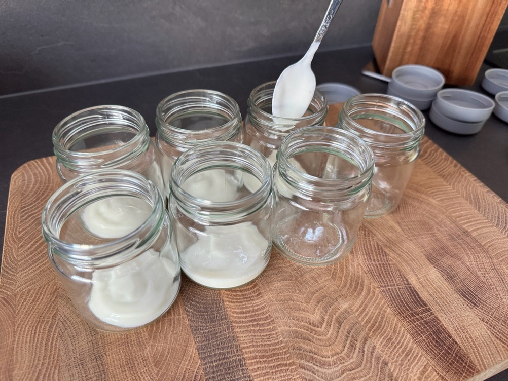 Eine Person gibt mit einem Löffel in jede Dose ein wenig Joghurt