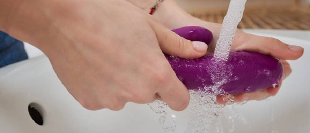 Sexspielzeug im Test: Frau, die einen Vibrator unter fließendem Wasser abwäscht