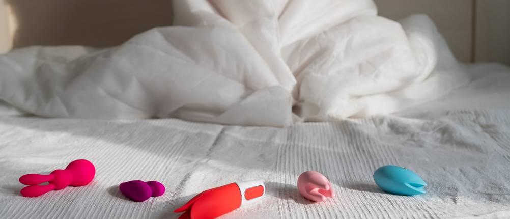 Sexspielzeug im Test: Bett, auf dem verschiedene Sexspielzeuge in bunten Farben liegen