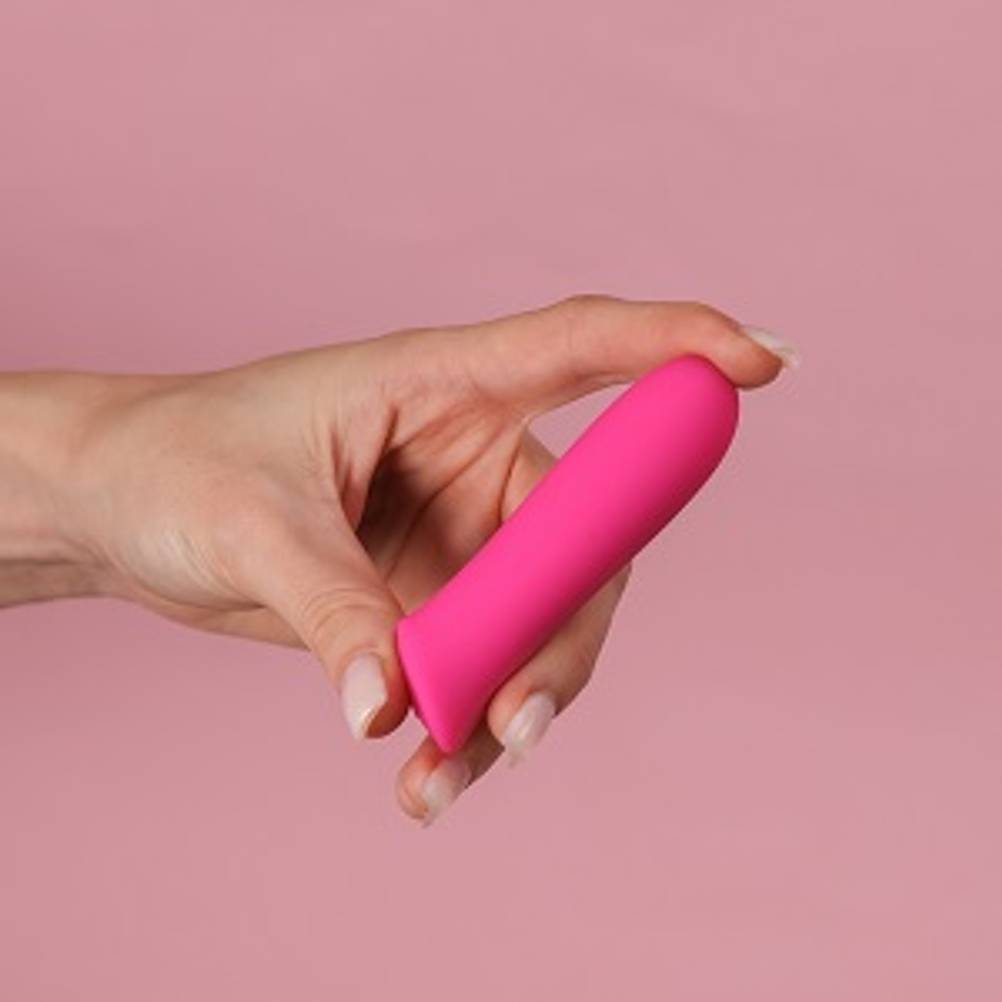 Sexspielzeug getestet: Kleiner pinker Vibrator, den eine Frau in der Hand hält, vor rosa Hintergrund