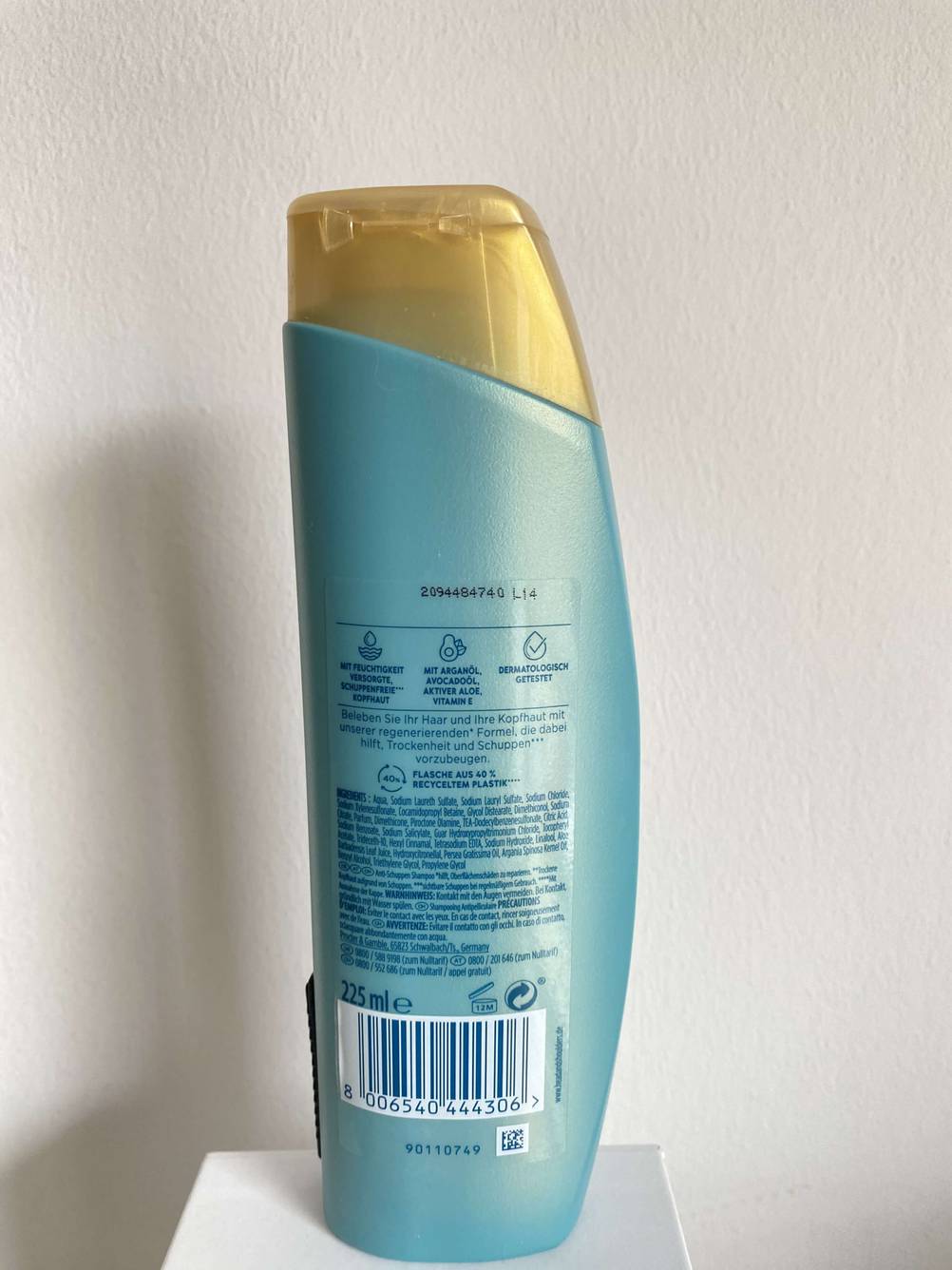 Rückseite einer Flasche getesteten Shampoos auf einem kleinen Sockel vor einer hellen Wand.