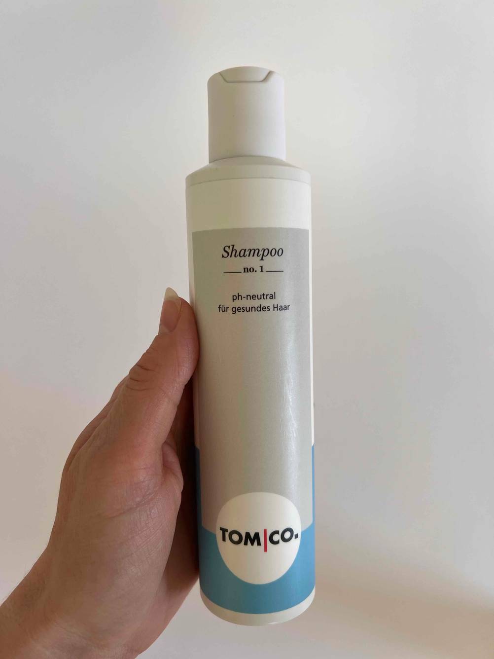 Eine Hand hält eine Flasche Shampoo ohne Silikone im Test vor eine helle Wand.