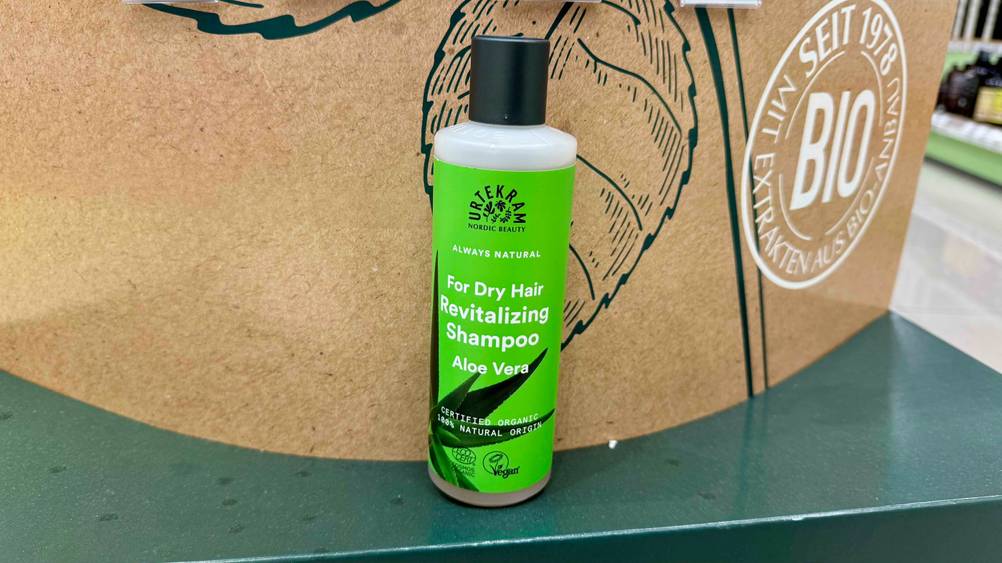 Vor einem Plakat steht eine Flasche des Shampoos für trockenes Haar im Test.