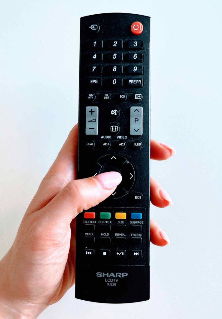 Getestete Universalfernbedienungen: Ein Damendaumen drückt die OK-Taste eines Modells von SHARP.