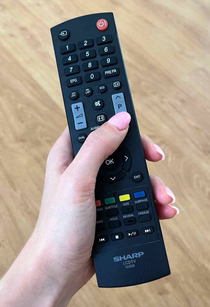 Universalfernbedienungen im Test: Ein Damendaumen drückt die Programmwahl-Taste eines schwarzen SHARP Modells.
