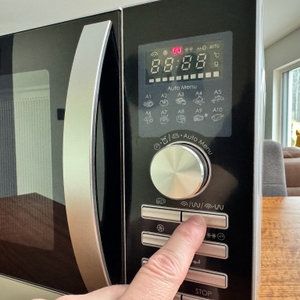 Eine Hand drückt einen Knopf bei der Sharp R843INW