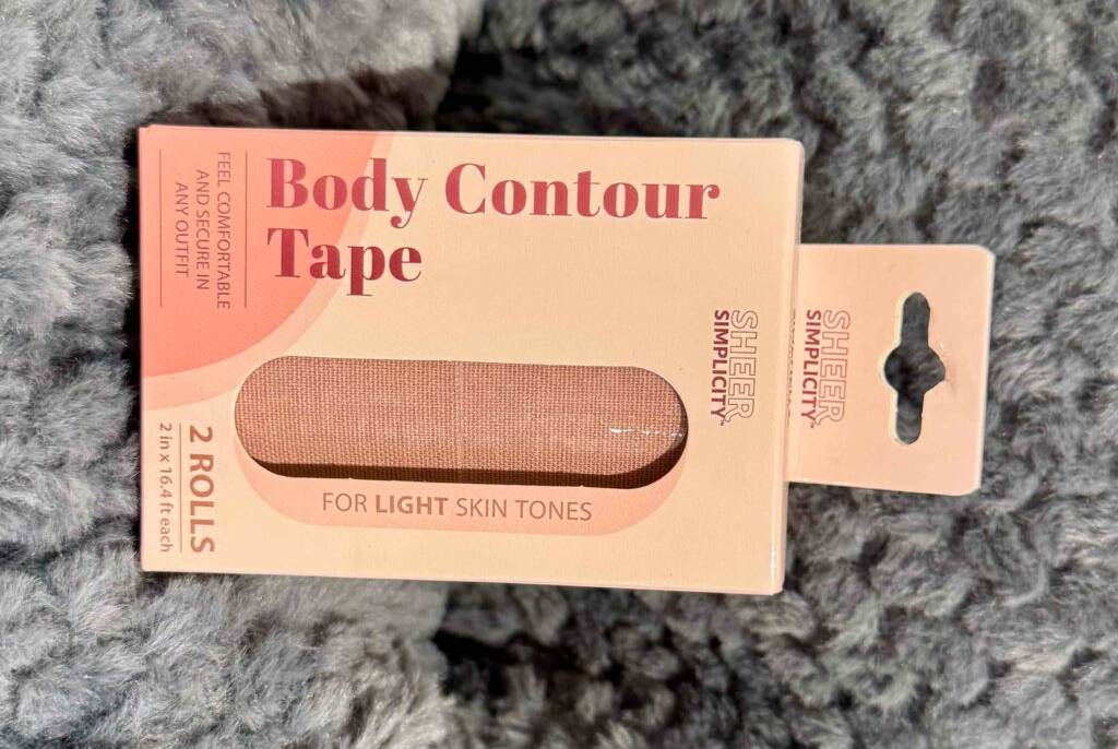 Das getestete Body-Tape besteht aus zwei Rollen Brust-Tape, die in einem Verpackungskarton mit Sichtfenster auf einem Plüschteppich liegen.