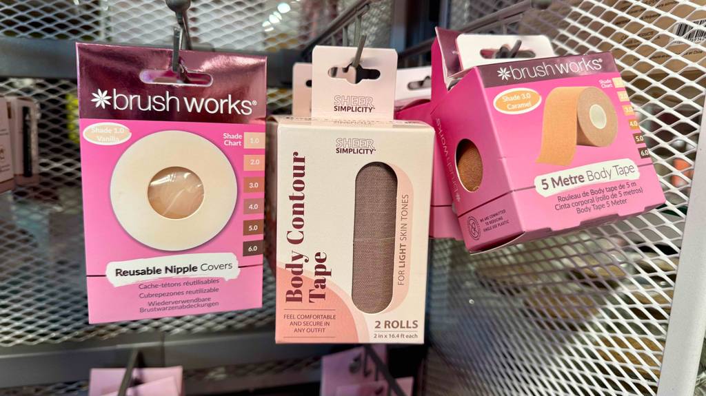 Im Test: Das Body-Tape in der Hautfarbe hängt innerhalb des Verpackungskartons mit Sichtfenster an einem Verkaufsregal neben weiteren Produkten für den Oberkörper.