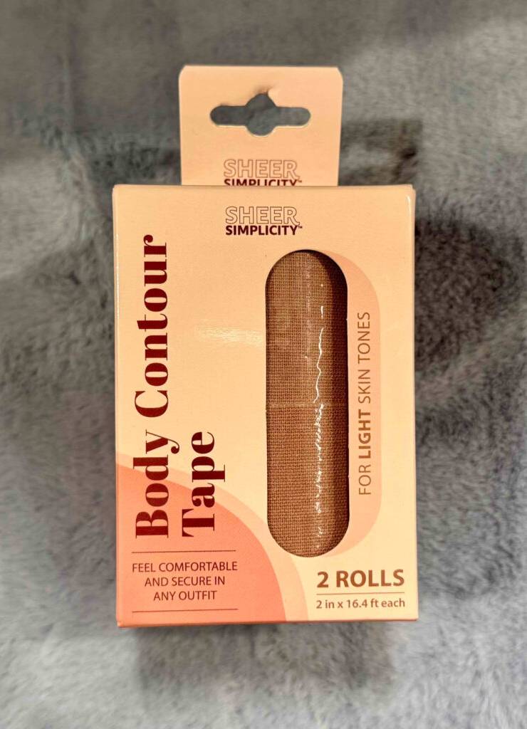 Body-Tape im Test: Zwei hautfarbene Rollen Brust-Tape liegen im Verpackungskarton mit Sichtfenster auf einem hellgrauen Plüschmaterial.