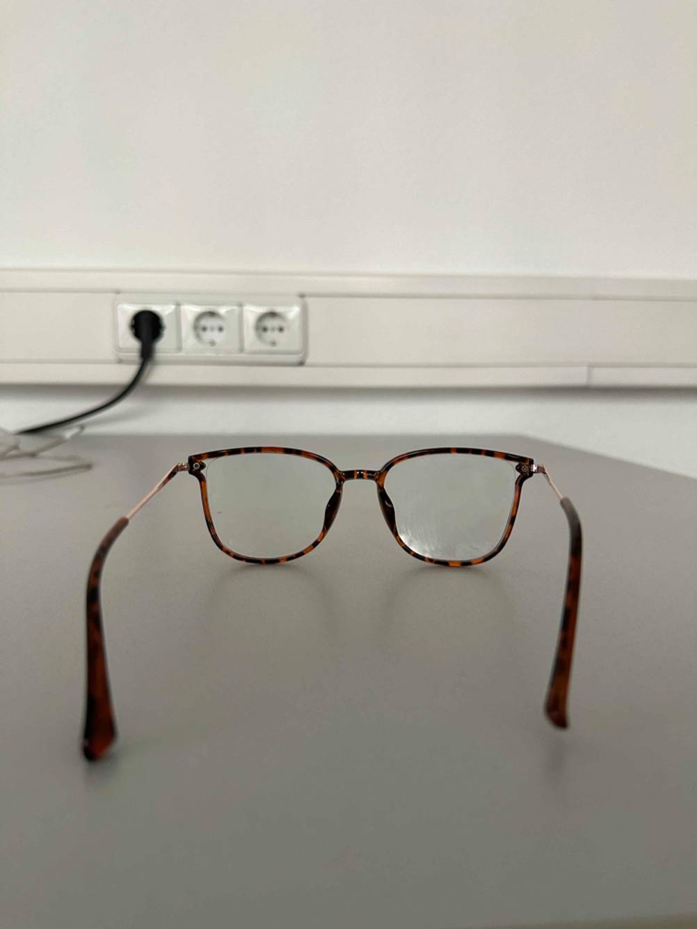 Nahaufnahme der verstärkten Bügel einer getesteten Blaulichtfilter-Brille mit Vollrahmen im Horn-Design, die vor einer weißen Wand inklusive Steckerleiste liegt.