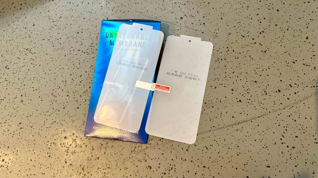 Eine blaue Verpackung mit einem Samsung-Galaxy-S21-Panzerglas im Test liegt auf einem gepunkteten beigefarbenen Boden.