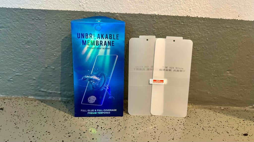 Eine blaue Verpackung mit zwei Samsung-Galaxy-S21-Panzerglasen im Test steht an einer braunen Wand.