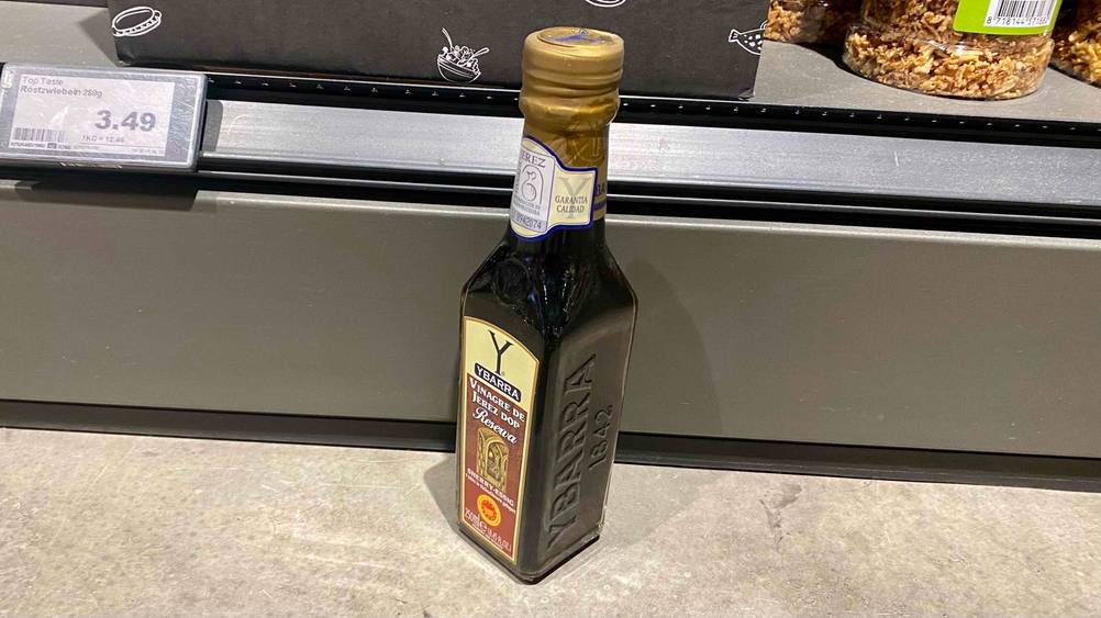 Sherryessig getestet: Seitenansicht einer Flasche die vor einem Regal steht.