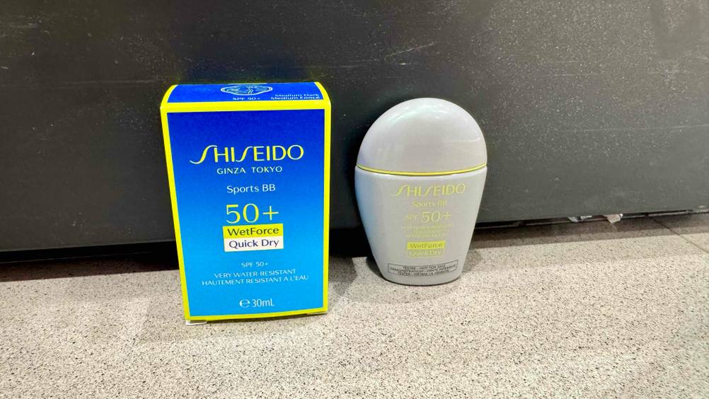 Der getestete Shiseido-Sonnenschutz neben der Originalverpackung vor einer grauen Wand.