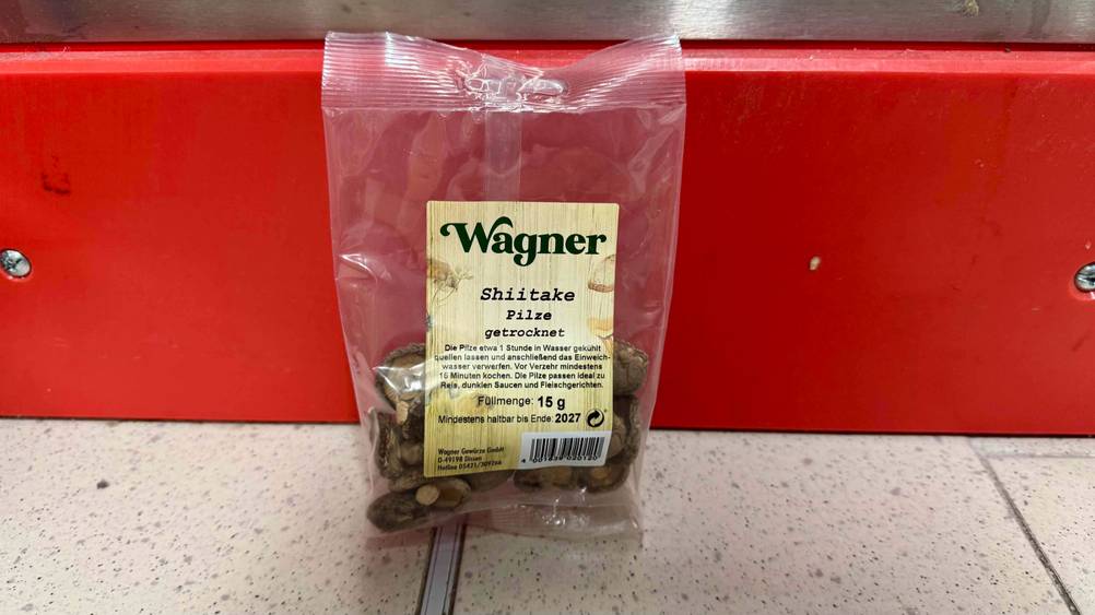 Eine Packung der getesteten Shiitake-Pilze vor einer roten Leiste auf dem Boden.