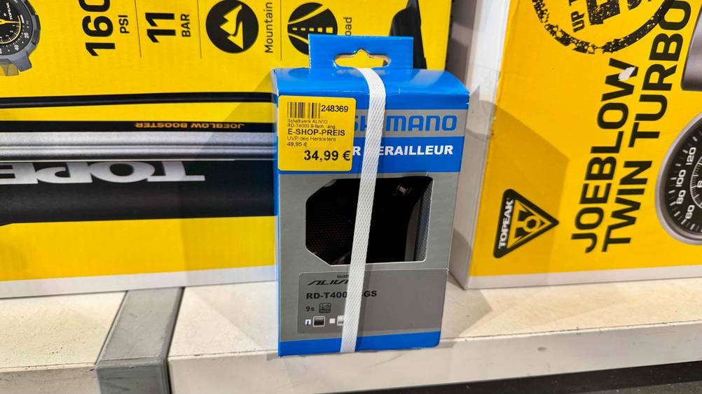 Ein getestetes Shimano-Schaltwerk vor Kartons auf einem Regalbrett.