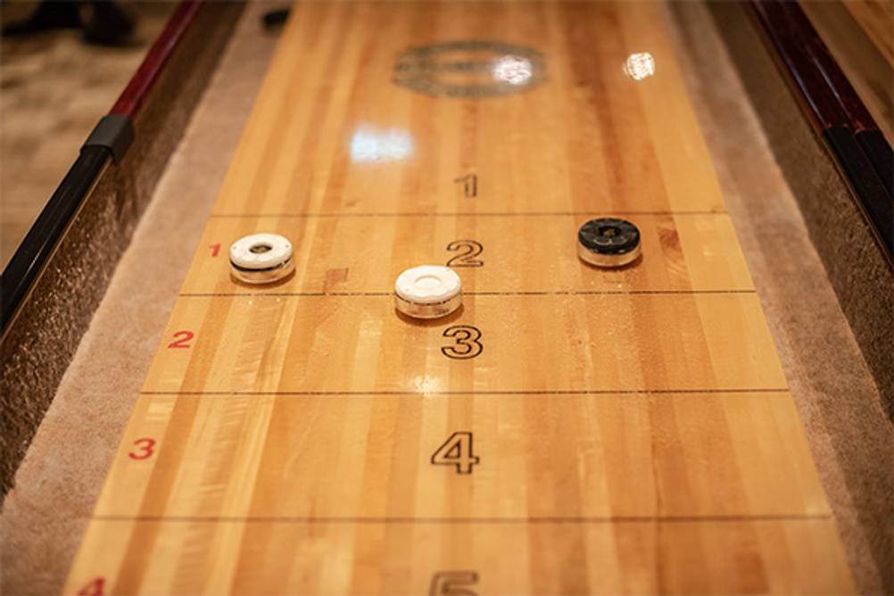 Shuffleboard im Test: Ein Tisch-Shuffleboard aus Holz mit Pucks
