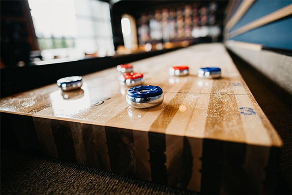 Shuffleboard im Test: Eine lange gewachste Shuffleboard-Spielfläche mit einigen Pucks.