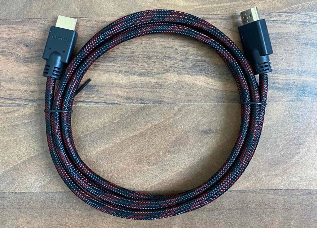 Ansicht von oben auf ein aufgerolltes, getestetes HDMI-Kabel mit 3 Meter Länge inklusive geflochtenem Überzug in Schwarz-rot. Darunter eine Holzoberfläche.