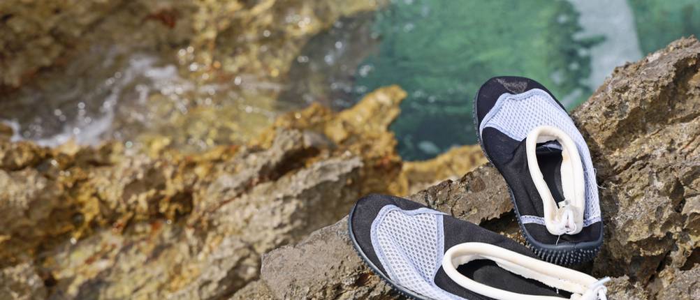 Badeschuhe für Erwachsene im Test: Badeschuhe, die am Rande einer Steinklippe liegen, darunter das Meer