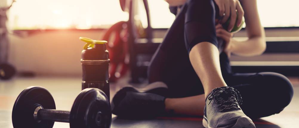Fitness-Handschuhe-Damen: Eine Frau sitzt am Boden in einem Fitnesscenter, vor ihr liegen Gewichte. 